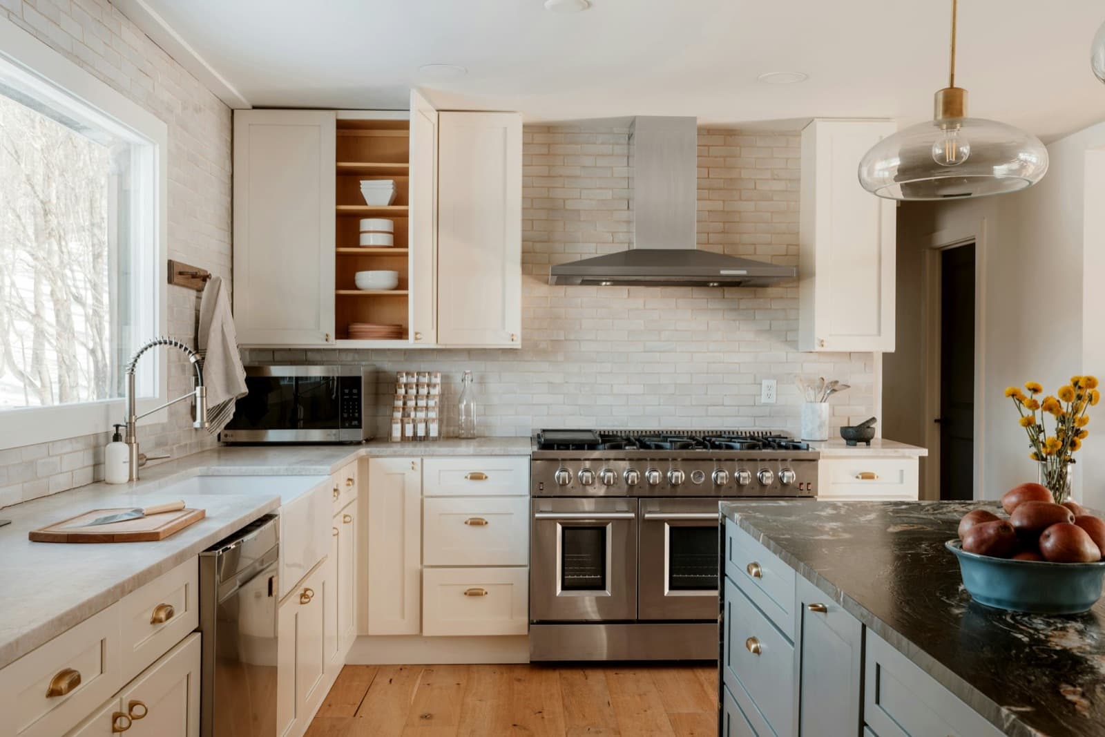 A bright renovated kitchen with white shaker cabinets, a stainless range and a dark stone island