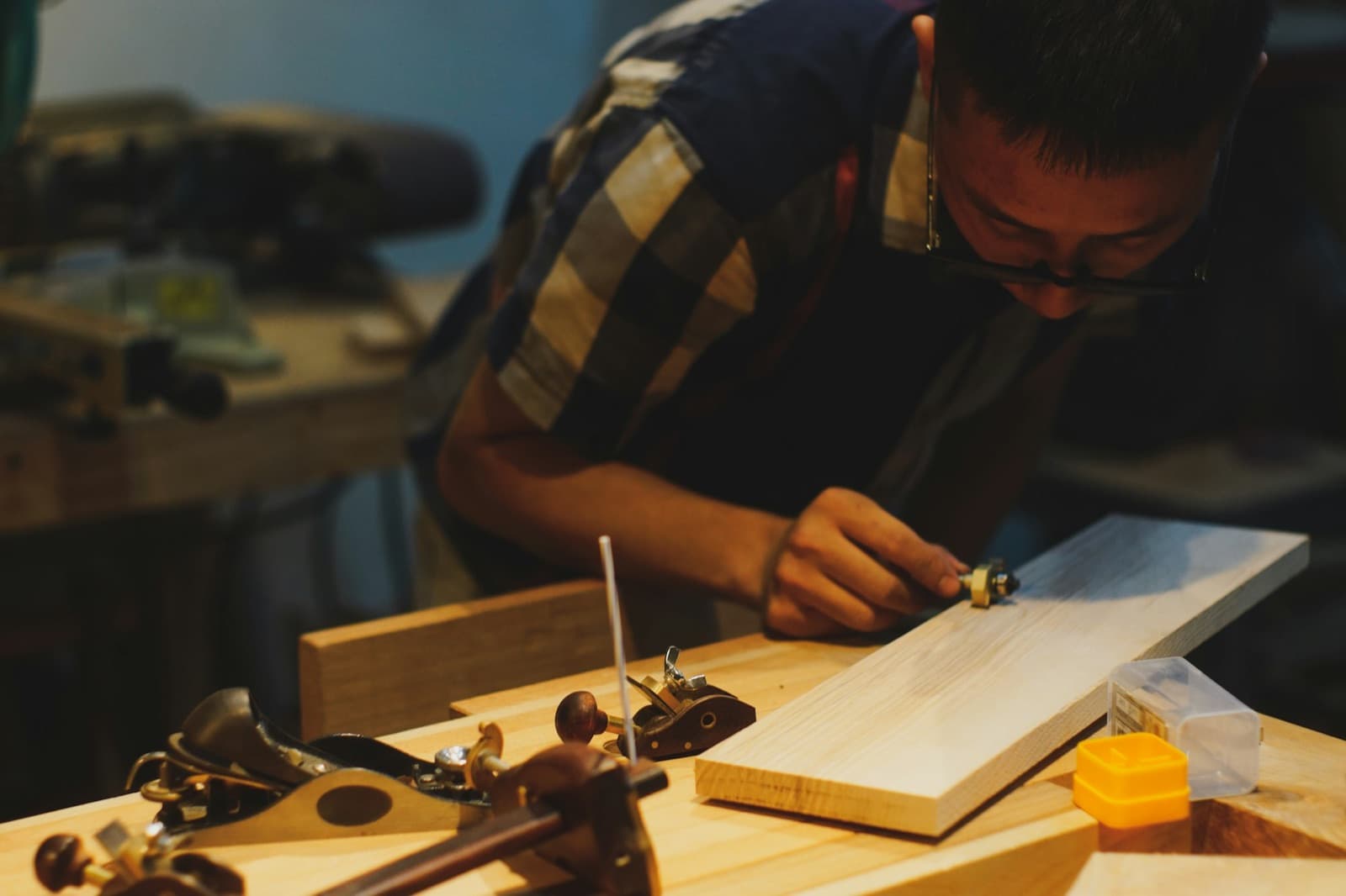 A carpenter shaping a board at a workbench beside hand planes